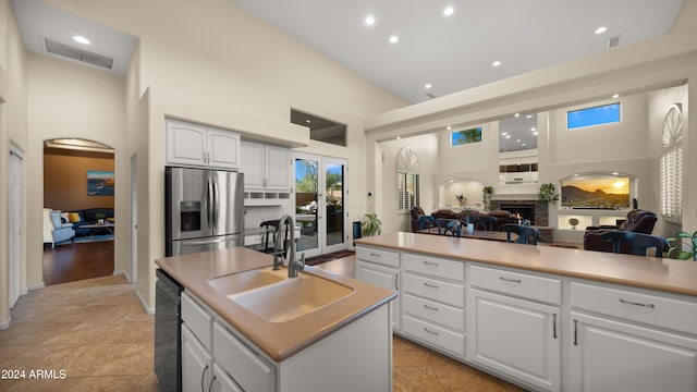 kitchen featuring white cabinetry, sink, stainless steel fridge with ice dispenser, a towering ceiling, and an island with sink