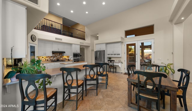 kitchen featuring backsplash, a high ceiling, appliances with stainless steel finishes, a kitchen bar, and white cabinetry