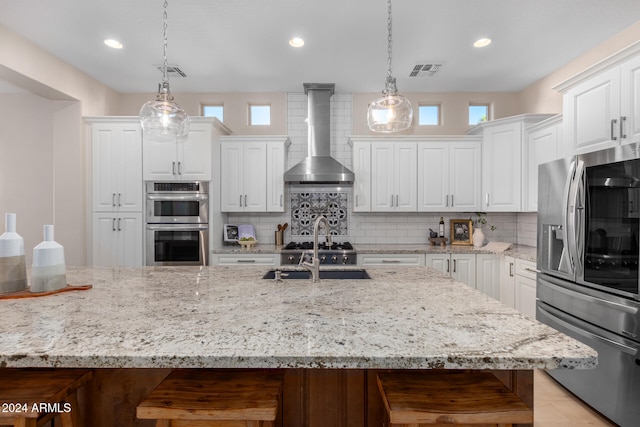 kitchen featuring stainless steel appliances, wall chimney exhaust hood, plenty of natural light, and hanging light fixtures