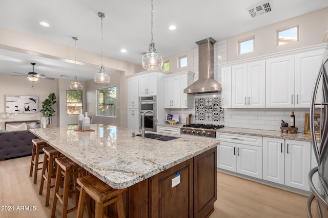 kitchen with white cabinets, wall chimney range hood, a kitchen island with sink, and stainless steel appliances