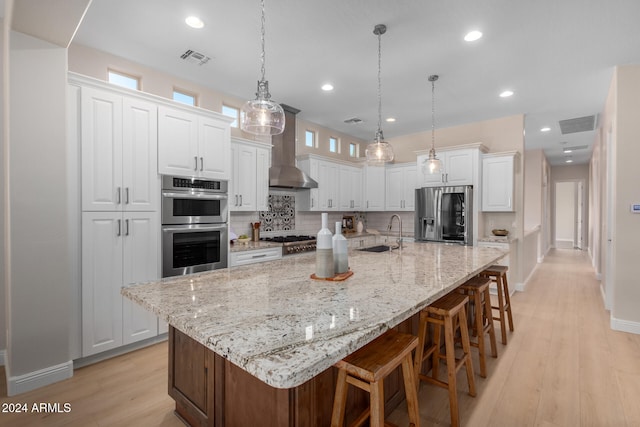 kitchen with pendant lighting, wall chimney exhaust hood, a large island, white cabinetry, and appliances with stainless steel finishes