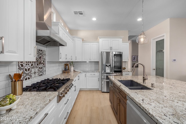 kitchen with stainless steel appliances, sink, white cabinets, wall chimney range hood, and light wood-type flooring