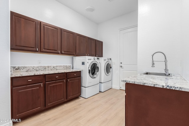 laundry area featuring cabinets, sink, light hardwood / wood-style flooring, and washer and clothes dryer