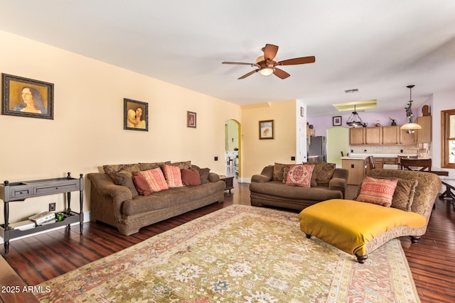 living room with arched walkways, ceiling fan, and dark wood-style floors