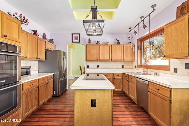 kitchen with dark wood-style flooring, appliances with stainless steel finishes, light countertops, decorative backsplash, and a kitchen island