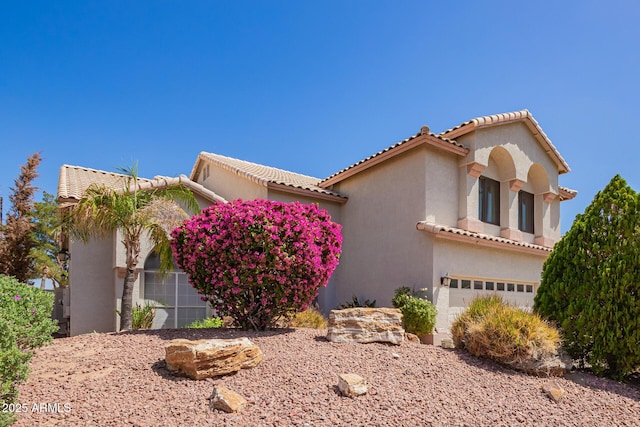mediterranean / spanish-style home featuring a tiled roof, a garage, and stucco siding