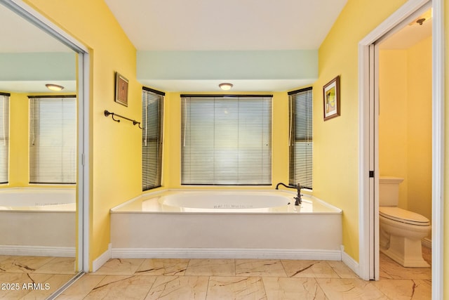 bathroom with a garden tub, marble finish floor, baseboards, and toilet