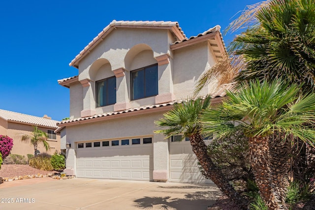mediterranean / spanish-style house featuring a garage, stucco siding, a tiled roof, and concrete driveway