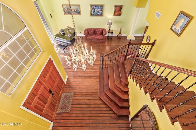 stairs with visible vents, a towering ceiling, wood finished floors, and a chandelier