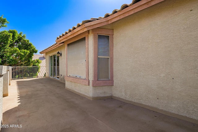 view of side of property featuring stucco siding, a patio area, and a tiled roof