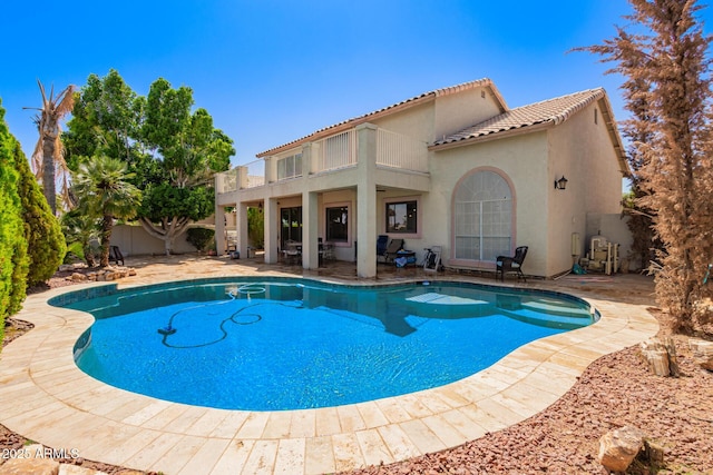 rear view of house with a tile roof, a fenced in pool, a balcony, a patio, and stucco siding
