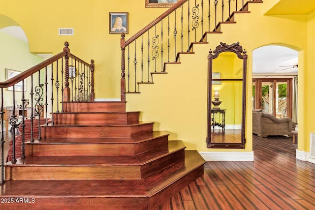 staircase featuring ceiling fan, visible vents, arched walkways, hardwood / wood-style flooring, and baseboards