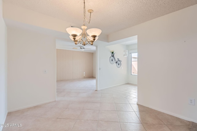 empty room with a chandelier, light tile patterned floors, a textured ceiling, and baseboards