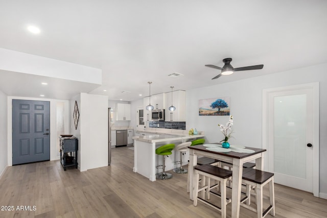 855 S Revolta Cir, Mesa, AZ 85208 - kitchen with a peninsula, stainless steel appliances, a breakfast bar, light wood-style flooring, and light countertops