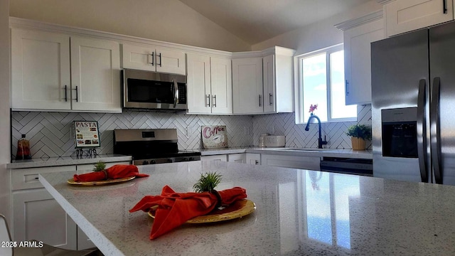 kitchen with lofted ceiling, backsplash, white cabinetry, and stainless steel appliances