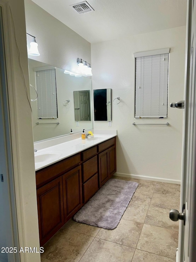 bathroom with baseboards, visible vents, a sink, and double vanity