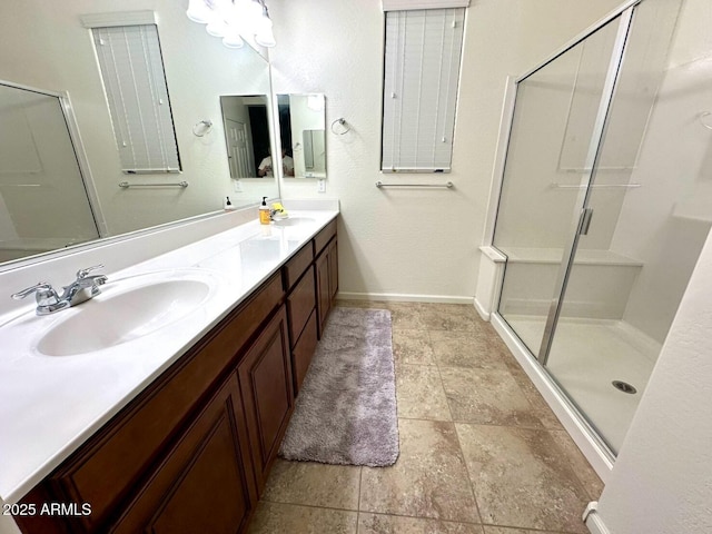 bathroom featuring a shower stall, double vanity, baseboards, and a sink