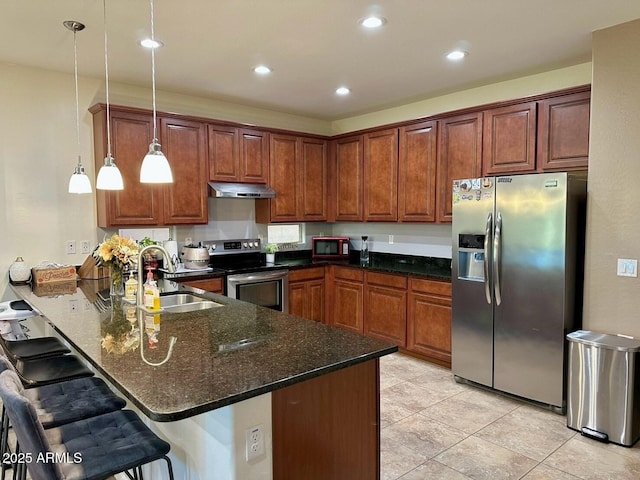 kitchen with a peninsula, stainless steel appliances, under cabinet range hood, a sink, and hanging light fixtures