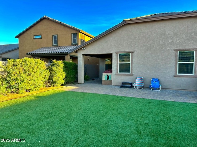 rear view of house with a tile roof, stucco siding, a patio area, and a lawn