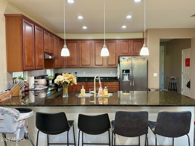 kitchen featuring stove, stainless steel refrigerator with ice dispenser, under cabinet range hood, a sink, and a peninsula