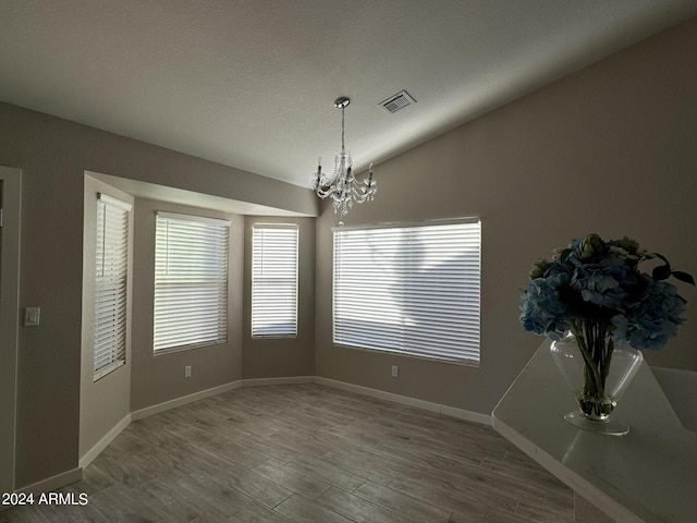 unfurnished dining area with hardwood / wood-style floors, lofted ceiling, and a notable chandelier