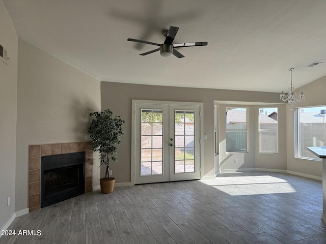 unfurnished living room featuring french doors, ceiling fan with notable chandelier, wood-type flooring, lofted ceiling, and a tiled fireplace