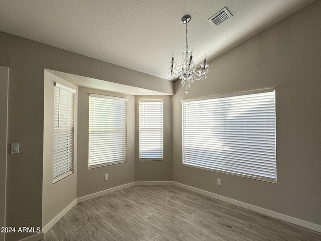 spare room with a textured ceiling, wood-type flooring, vaulted ceiling, and a notable chandelier