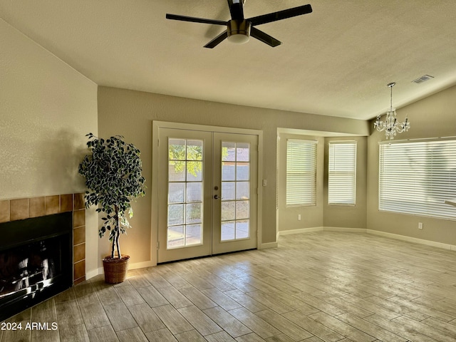 doorway to outside with french doors, ceiling fan with notable chandelier, a textured ceiling, and vaulted ceiling