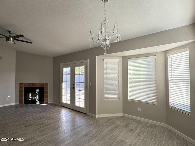 unfurnished living room featuring french doors, a tile fireplace, plenty of natural light, and ceiling fan with notable chandelier