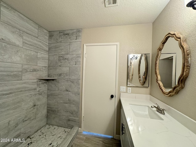 bathroom with a tile shower, vanity, and a textured ceiling