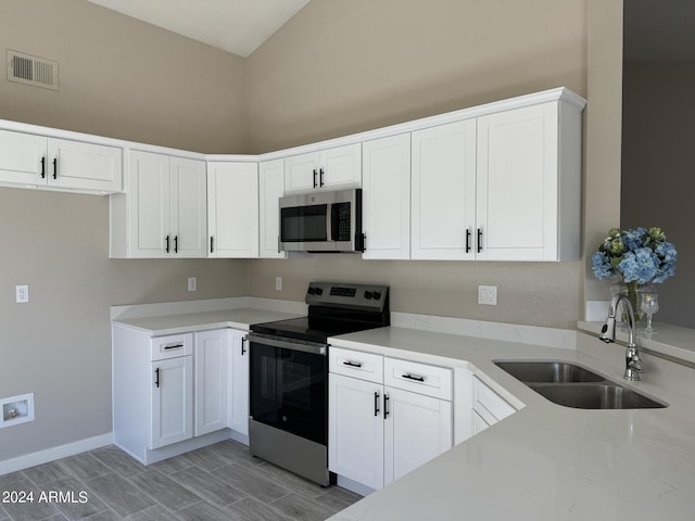 kitchen featuring white cabinets, stainless steel appliances, light stone counters, and sink