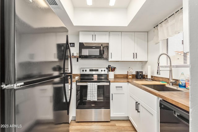 kitchen with black dishwasher, electric range, freestanding refrigerator, white cabinetry, and a sink