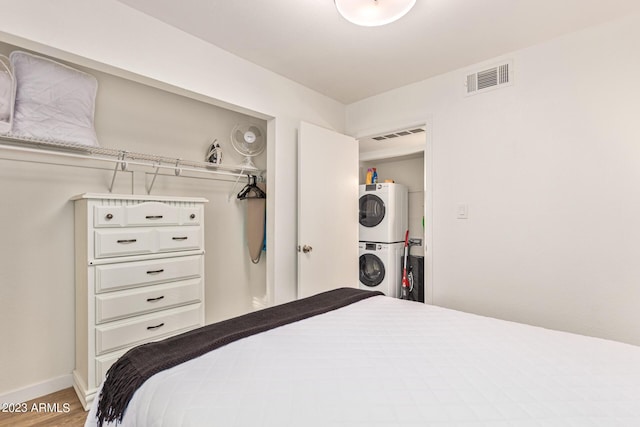 bedroom with stacked washing maching and dryer, baseboards, visible vents, and wood finished floors