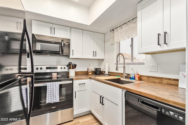 kitchen featuring black appliances, butcher block countertops, white cabinets, and a sink