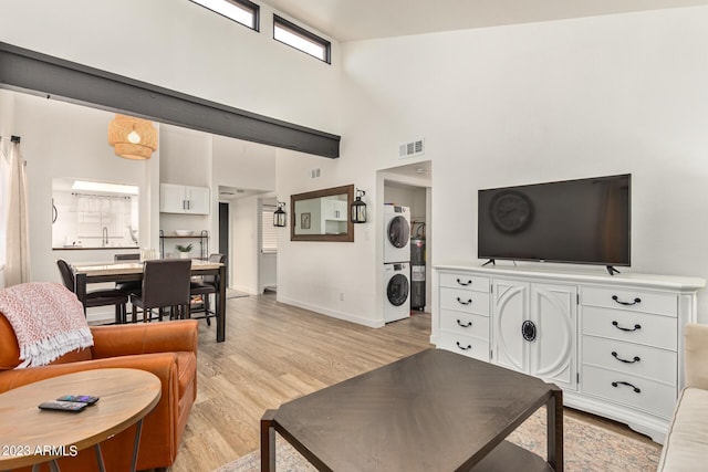 living area featuring light wood-style flooring, stacked washer and dryer, visible vents, a towering ceiling, and baseboards