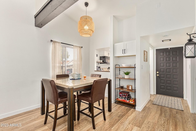 dining space with light wood-style flooring, high vaulted ceiling, and baseboards