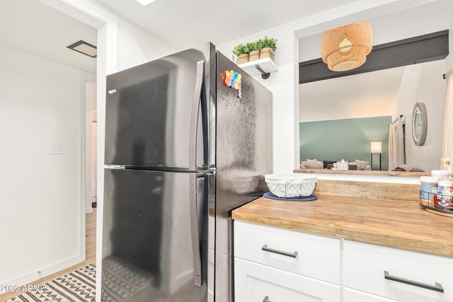 kitchen featuring wood finished floors, wood counters, baseboards, white cabinets, and freestanding refrigerator