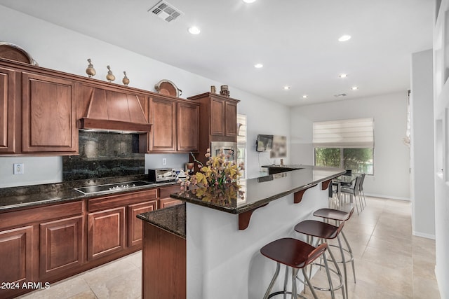 kitchen featuring dark stone counters, a kitchen breakfast bar, a kitchen island, tasteful backsplash, and stovetop