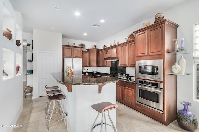 kitchen with appliances with stainless steel finishes, a breakfast bar, custom range hood, dark stone countertops, and a kitchen island