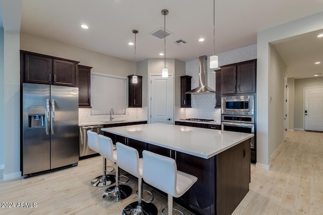 kitchen featuring visible vents, a sink, appliances with stainless steel finishes, wall chimney range hood, and dark brown cabinets