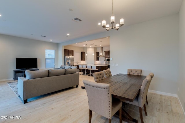 dining room featuring light wood-style flooring, a notable chandelier, baseboards, and visible vents