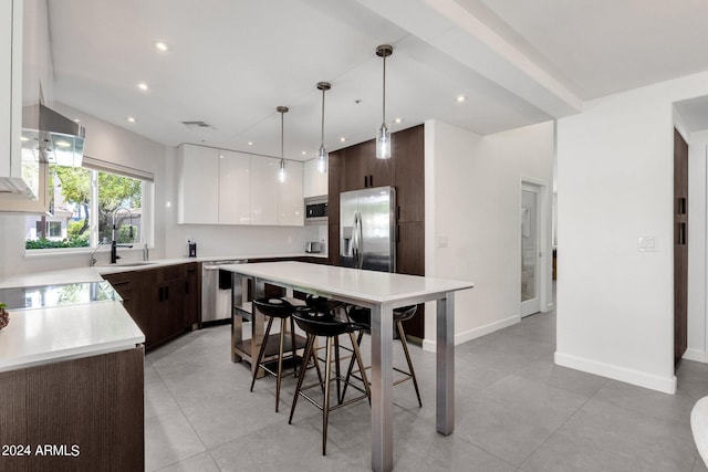 kitchen featuring decorative light fixtures, light tile flooring, stainless steel appliances, white cabinetry, and a center island