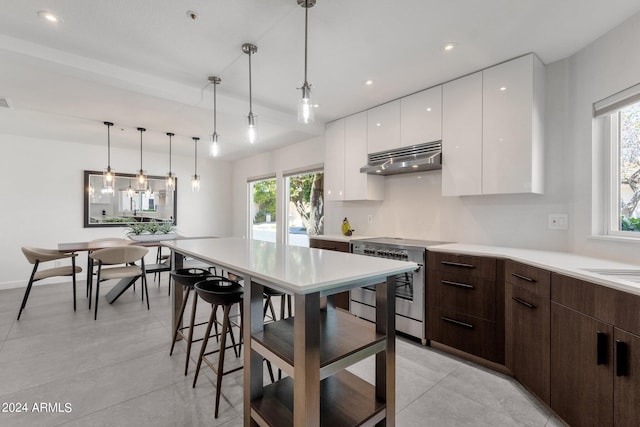 kitchen with dark brown cabinets, ventilation hood, decorative light fixtures, light tile floors, and high end stainless steel range