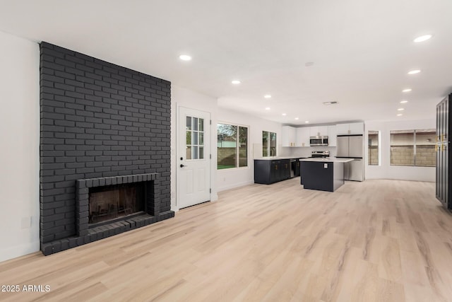 kitchen with a center island, a fireplace, light countertops, appliances with stainless steel finishes, and light wood-style floors