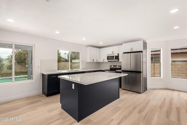 kitchen with a kitchen island, a sink, light countertops, appliances with stainless steel finishes, and light wood-type flooring