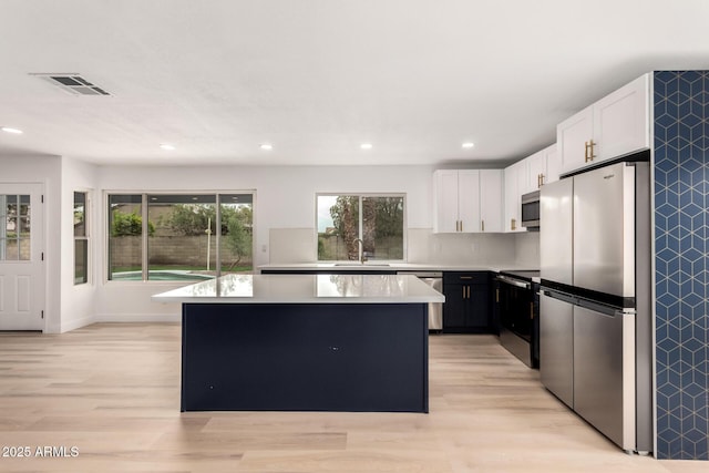 kitchen with stainless steel appliances, light countertops, light wood-style floors, a kitchen island, and a sink