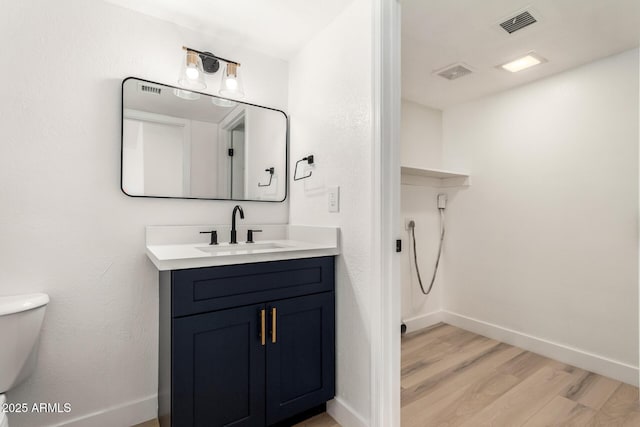 half bath with toilet, wood finished floors, visible vents, vanity, and baseboards