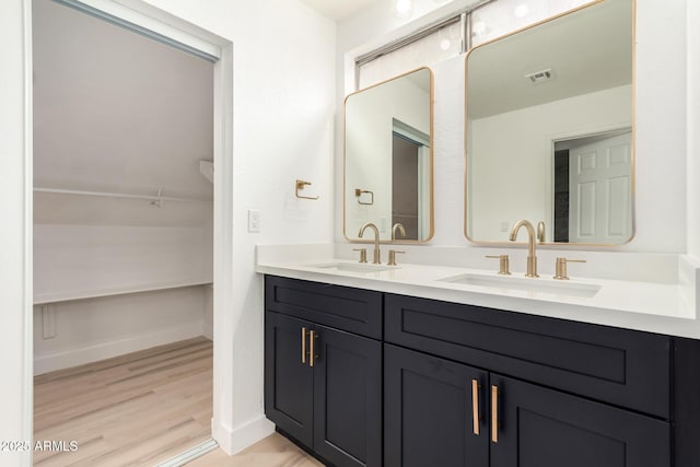 full bathroom with double vanity, visible vents, a sink, and wood finished floors