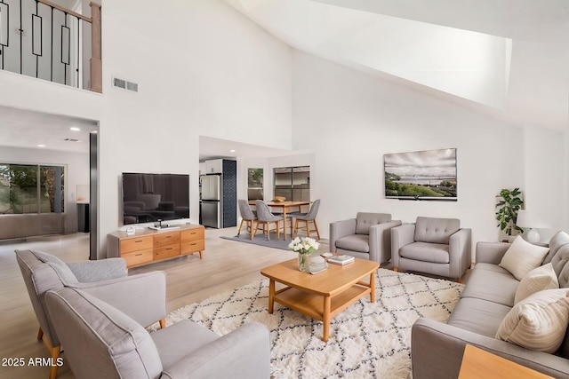 living room featuring high vaulted ceiling, light wood-type flooring, and visible vents