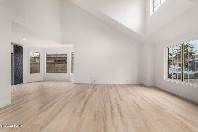 unfurnished living room featuring light wood-type flooring, a towering ceiling, and baseboards